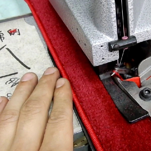 Close-up of a carpet overlocking machine finishing the edge of a red rug.