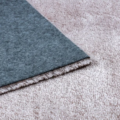 Close-up of a gray felt rug pad on a light beige plush carpet.