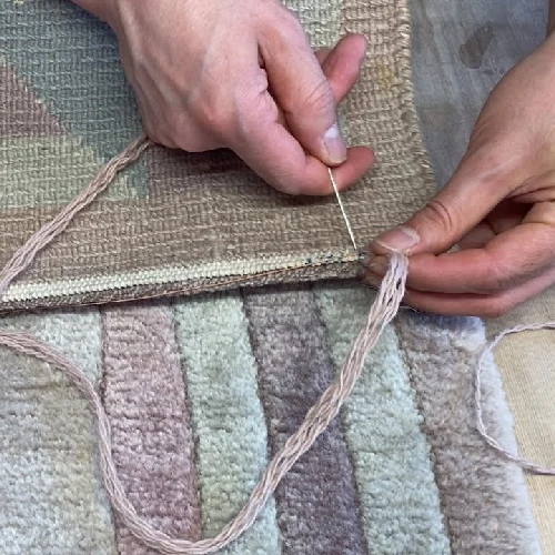 Hand-stitching a rug edge with needle and thick pink thread.