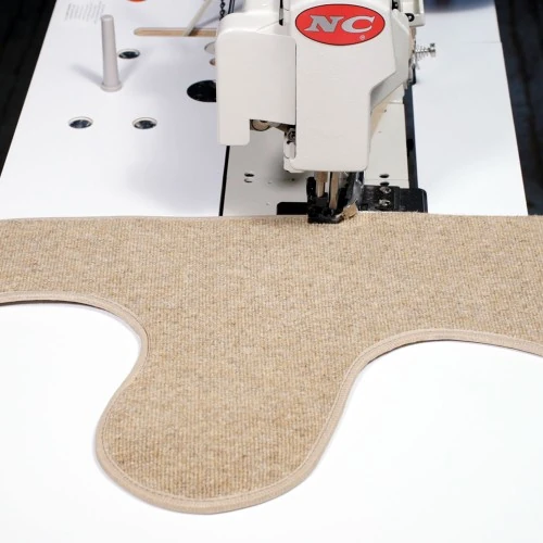 Industrial machine binding the edge of a custom-cut beige carpet.