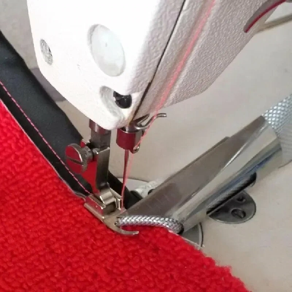 Industrial sewing machine stitching black tape binding onto a bright red rug.