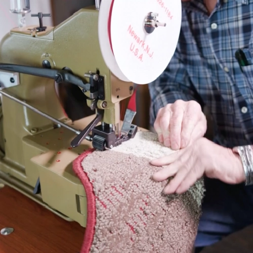 Professional carpet binder applying red tape to a textured rug edge.