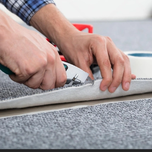 Trimming the edge of a gray loop pile carpet with a utility knife.