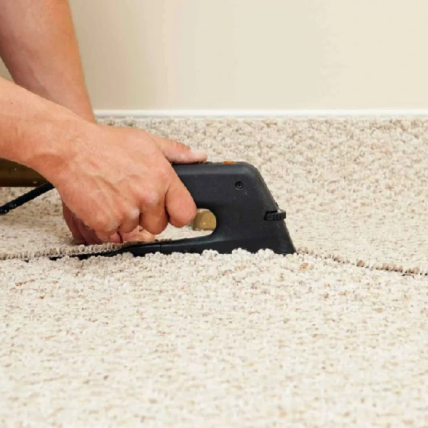 professional using an electric carpet cutter to trim a beige plush carpet.